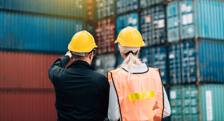 Two terminal workers in safety gear inspecting stacked shipping containers at a logistics yard.